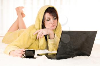 Woman in robe with laptop and cup lying on the floor