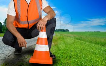 Royalty Free Photo of a Road Worker Kneeling With a Pylon 
