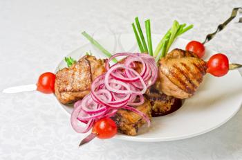 Grilled kebab meat with onion and tomato on a white plate