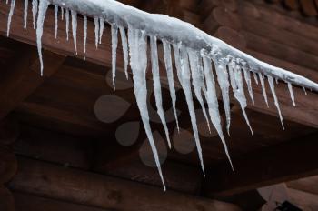 Closeup photo of the Icicles hang from the roof of wooden house
