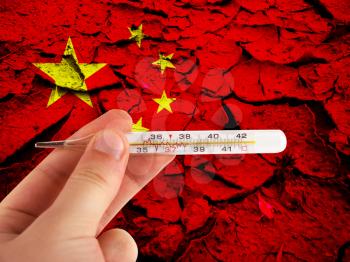 Hand with a medical thermometer on China cracked earth background. Concept of corona virus.