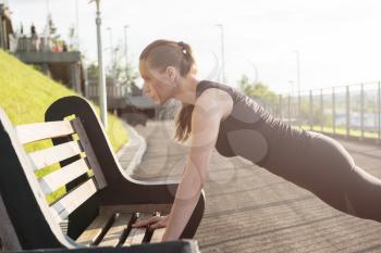 A woman in sportswear doing push ups in the city park in sunny evening.