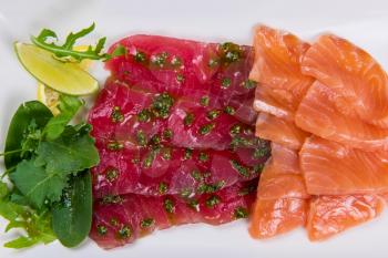 Mixed sliced fish: salmon and tuna decorated with greens and lemon in white plate