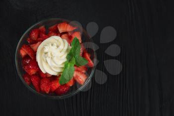 Strawberry with cream decorated with mint leaf on black wooden background