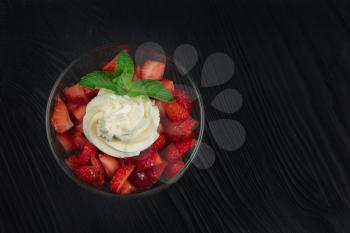 Strawberry with cream decorated with mint leaf on black wooden background
