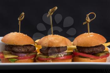 Three mini hamburgers, mini burgers closeup on plate on dark background