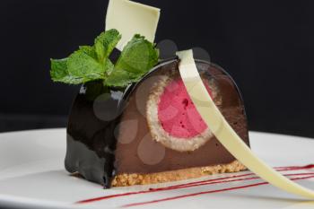 Delicious biscuit chocolate cake closeup with pink souffle decorated with mint and white chocolate on dark background