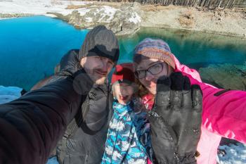Family selfie at winter journey. Mother, father and son taking selfie photo in forest at beauty sunny winter day, in Altai mountains. Travel vacation concept.
