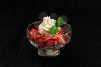 Strawberry with cream decorated with mint leaf on black wooden background, food and drink concept
