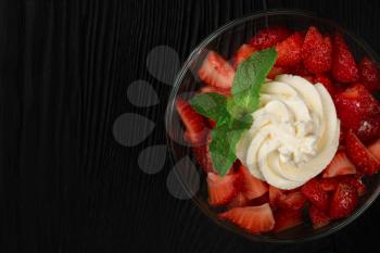 Strawberry with cream decorated with mint leaf on black wooden background, with copyspace, food and drink concept