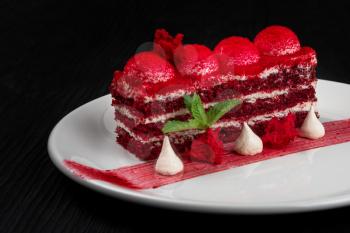 Plate with piece of delicious red velvet cake on black wooden background, food and drink concept