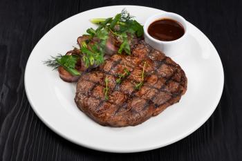 Grilled black angus steak ribeye on white plate on black wooden background