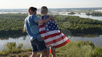 Father with American flag embraces his son on river bank. Patriotism, independence day 4th july concept