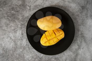 Fresh yellow mango fruit in a black plate on grey stone backgrounds
