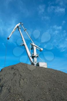 crane at heap of gravel on blue sky background