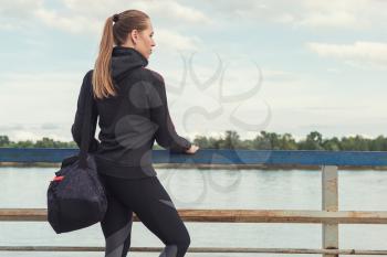 A woman in sportswear with bottle of water on embankment background