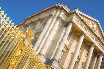 Palace facade with columns and golden gate in Versailles over blue sky. France