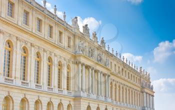 Palace side with statues on top in Versailles over blue sky. France