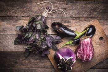 Rustic style Aubergines and basil on chopping board  and wooden table. autumn food photo