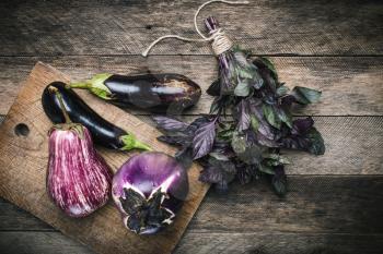 Aubergines and basil on chopping board and wooden table. Rustic style and autumn food photo