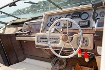 A view of the steering wheel and dashboard controls of the old motor boat, docked in the marina.