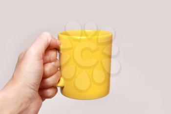 Hand holding yellow mug isolated on beige background

