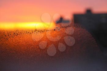 Background with ice, morning sunlight and silhouettes of houses on winter window glass
