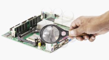 Human hand holding magnifying glass over a circuit board