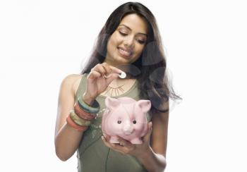 Young woman putting a coin into a piggy bank