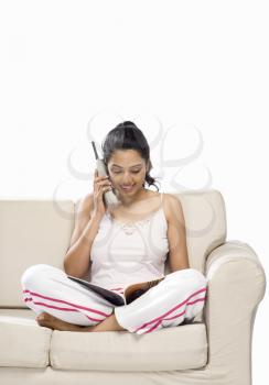 Young woman talking on a cordless phone and looking at a magazine