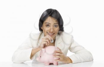 Businesswoman inserting a coin into a piggy bank