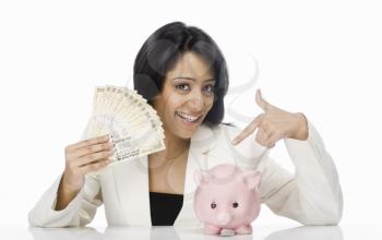 Businesswoman holding Indian paper currency and piggy bank
