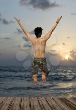 Rear view of a young man jumping with joy over a pier