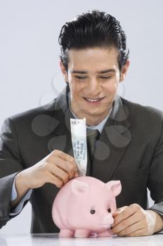 Businessman putting one hundred rupees note in a piggy bank