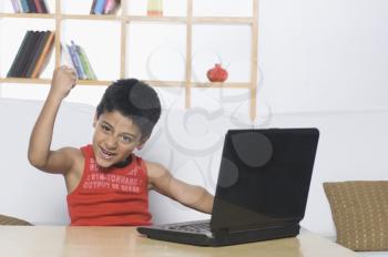 Portrait of a boy working on a laptop and clenching his fist
