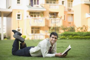 Portrait of a businessman lying on the grass and reading a book