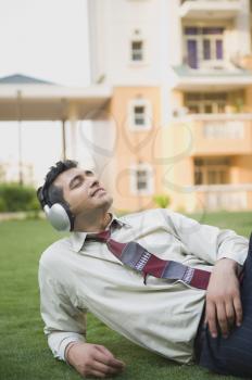 Businessman lying on the grass and listening to music