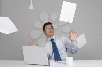 Businessman sitting in office with papers falling around him