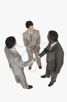 Two businessmen shaking hands with another businessman standing beside them