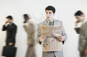 Businessman reading a newspaper with his colleagues in the background