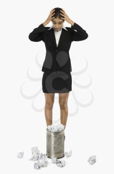 Businesswoman standing in front of a wastepaper basket and holding her head