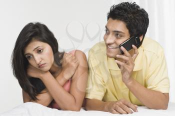 Man talking on a mobile phone with a woman looking sad beside him