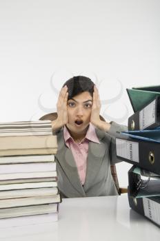 Stack of books and binders in front of a businesswoman at desk