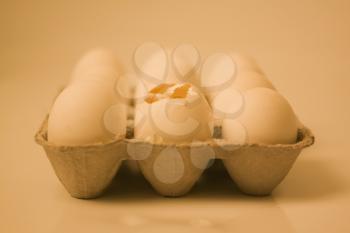 Broken egg in a carton with other eggs