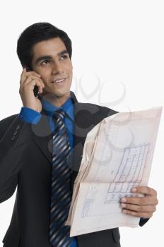 Real estate agent holding a blueprint and talking on a mobile phone