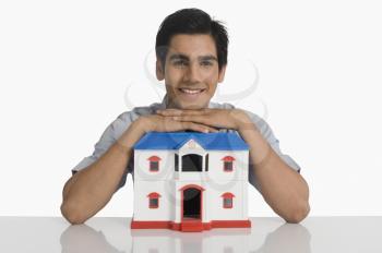 Real estate agent leaning on a model home and smiling