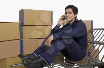 Store incharge sitting on a hand truck and talking on a mobile phone