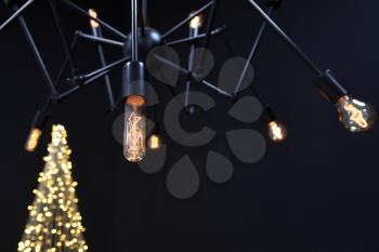 New year's Loft-style decor against a black wall, a Christmas tree from a garland. black chandelier with incandescent lamps. Beautiful New Year's decor with lighting in the studio.