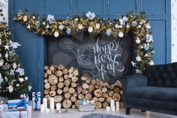 Beautiful decor of the holiday happy new year with prepared wood for the fireplace and the inscription of a happy new year, written in chalk.