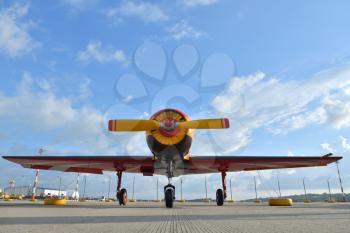 Beautiful yellow piston aircraft with a propeller is parked at the airport against a blue sky with clouds